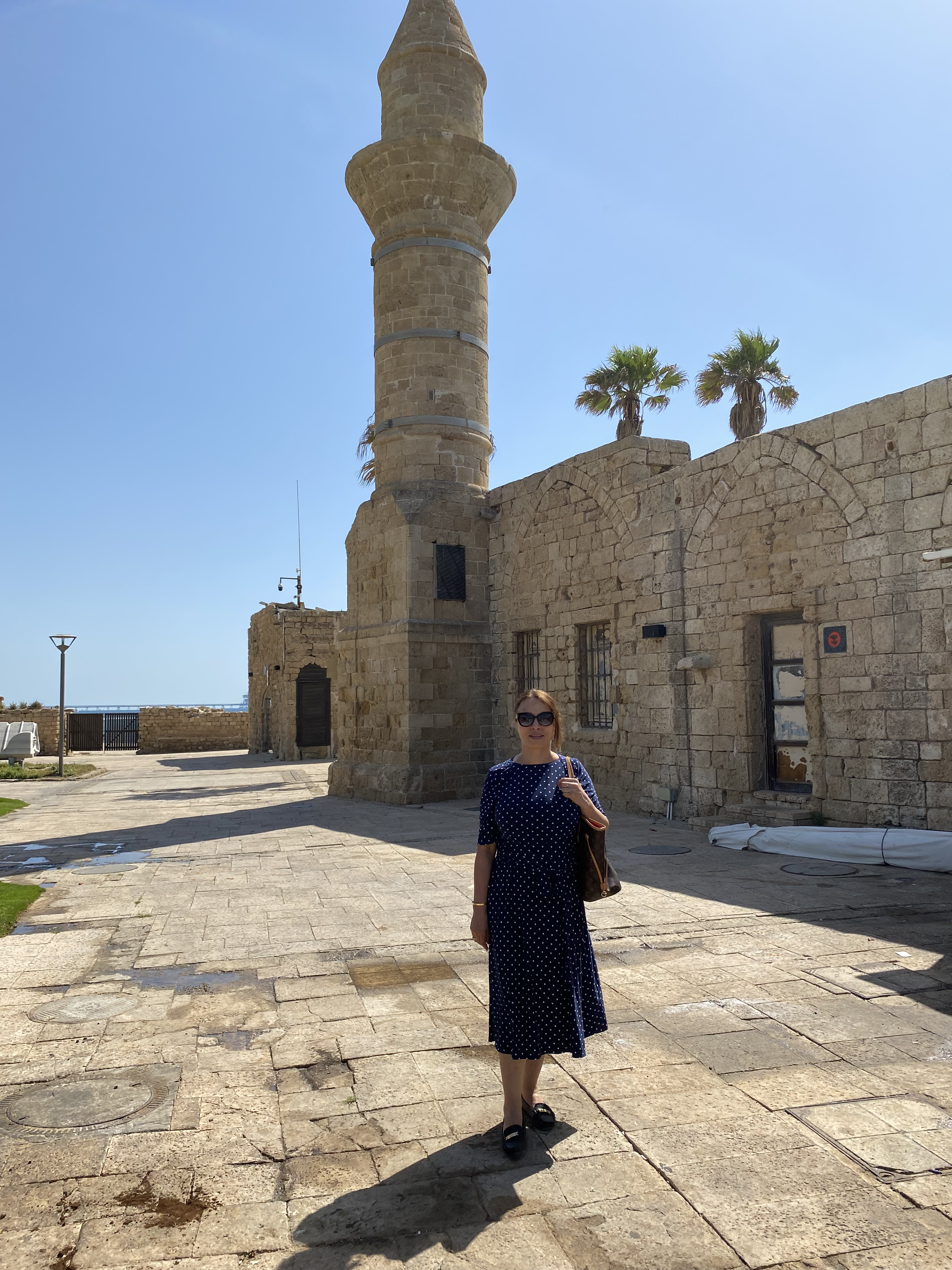 A woman standing in front of an old mosque with a minaret in Caesarea